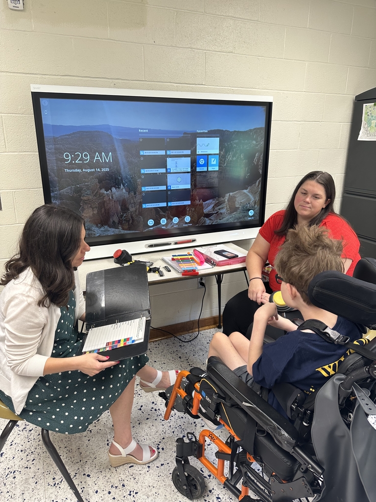 Ms. Ashley Suddath, Speech Language Pathologist, Ms. Jasmine Morgan, Occupational Therapist sit on either side of a male student in a wheelchair during his session.