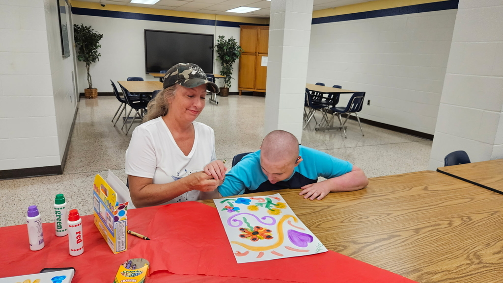 A female Residential Care Specialist assists a male student with an art activity. They are drawing colorful flowers and hearts.