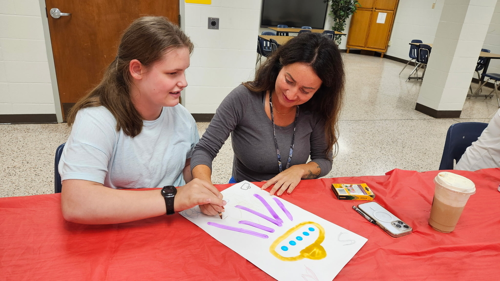 A female Residential Care Specialist assists a female student with an art activity. They are coloring a spaceship.