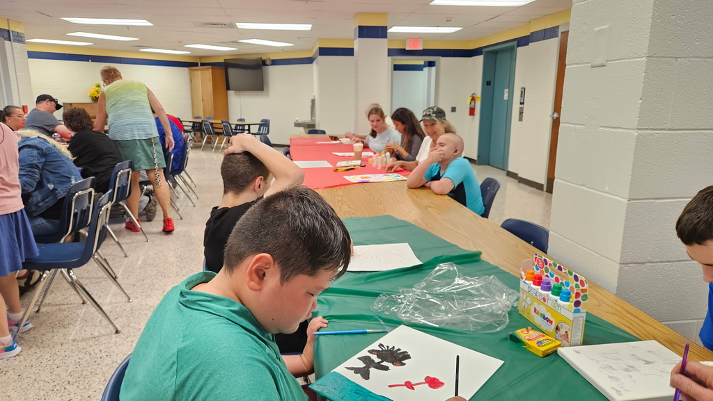 Students seated at a long, rectangular table full of art supplies as they work on their art activity.