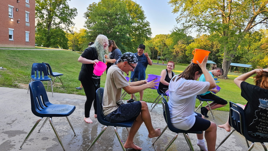 Students seated while they use bright colored buckets that are filled with water to dump onto one another.