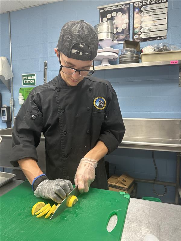 A male student looks down as he cuts yellow lemons on top of a green cutting board.