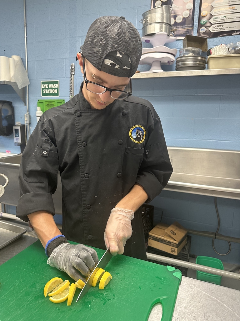 A male student looks down as he cuts yellow lemons on top of a green cutting board.