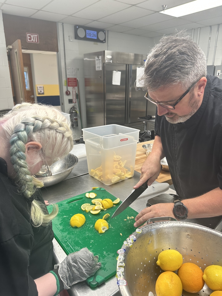 Chef Brian Olden stands across from a female student as he demonstrates the proper way to cut fruit.