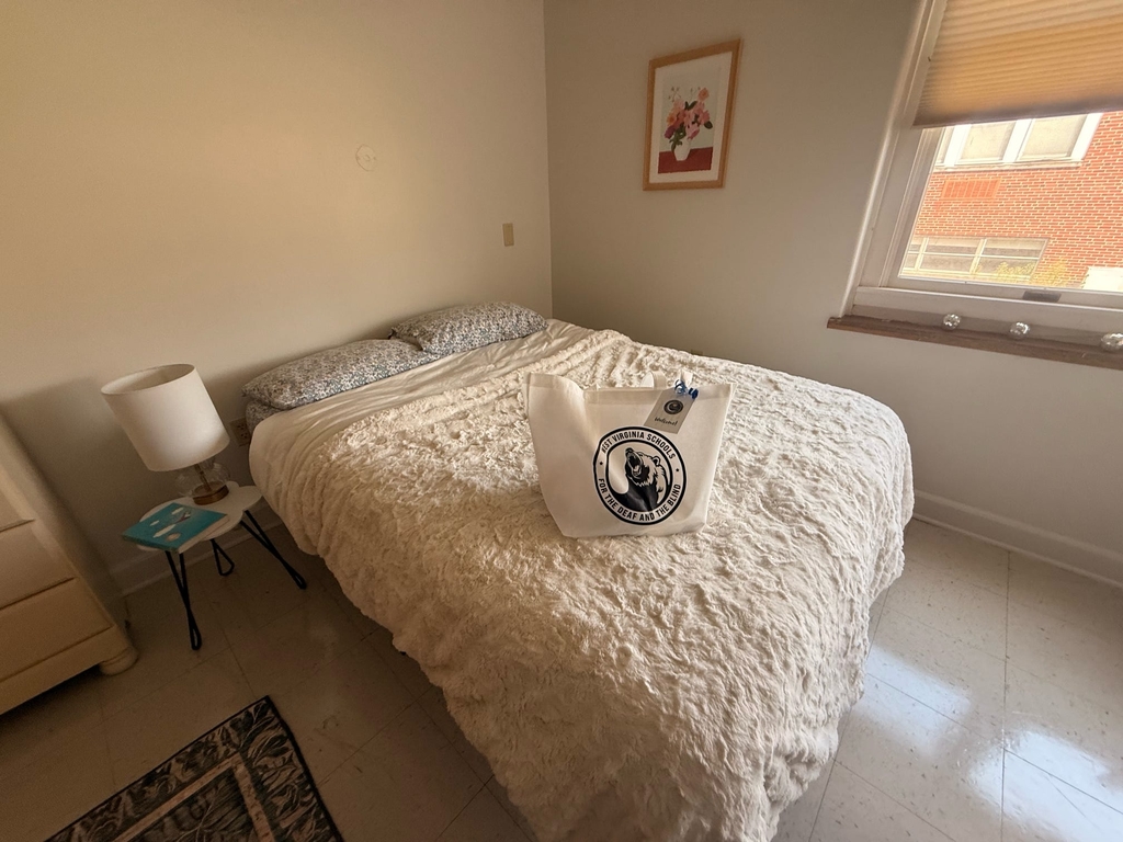 Staged CAP dorm room featuring a bed with a white comforter and white WVSDB bag with the Black Bear logo.