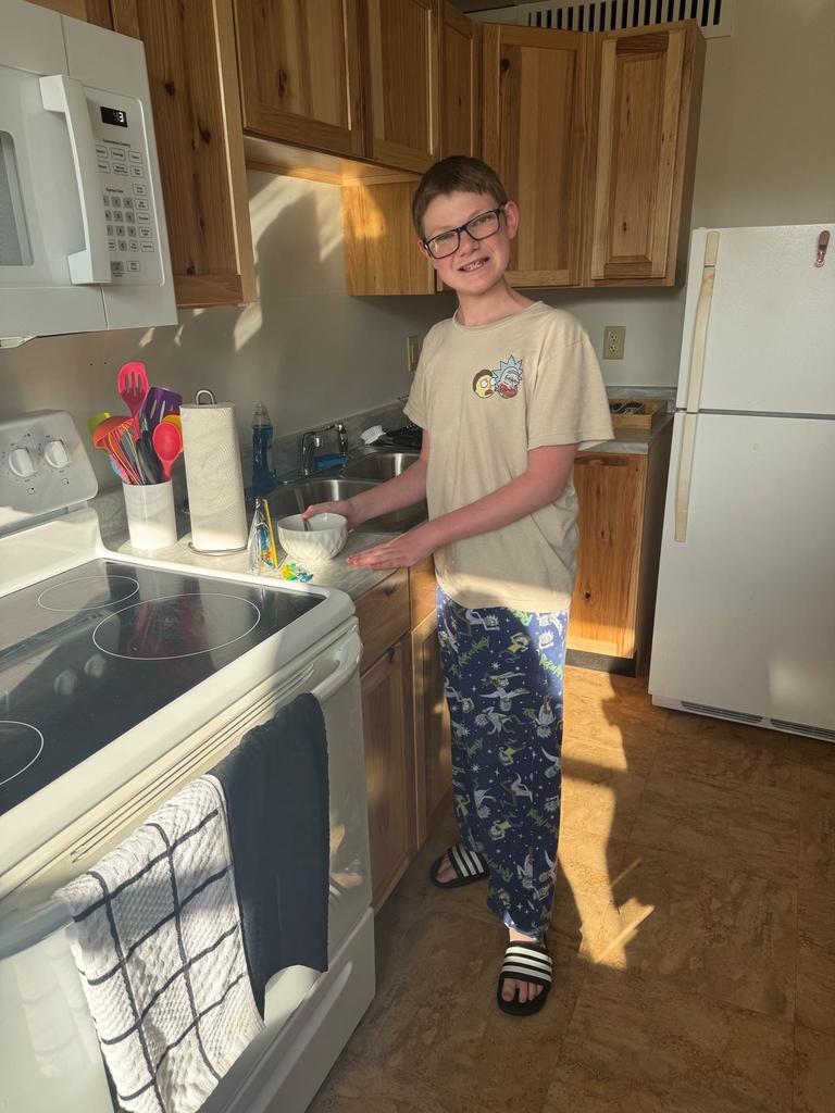 A male CAP student smiles at the camera as a bowl of cereal sits on the kitchen counter in front of him.