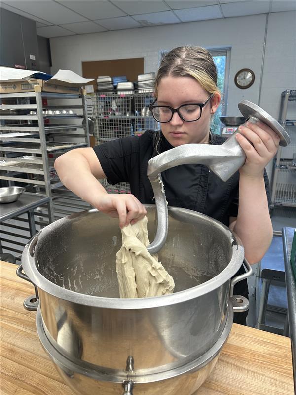 Bindi, a female student takes freshly mixed dough out of a large metal bowl.