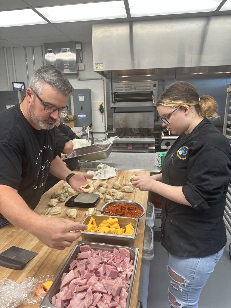 Chef Olden stands across from a female student as they put various ingredients into dough.