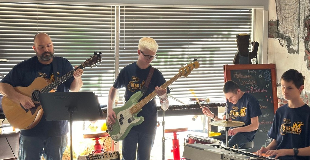 Male WVSDB Rock Band musicians stand on a stage with their instruments alongside music teacher, Mr. Haza.