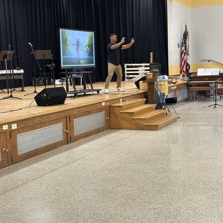 Justin Perez stands on a stage with his hands out in front of him. A large smart board is behind him with a dog on it.