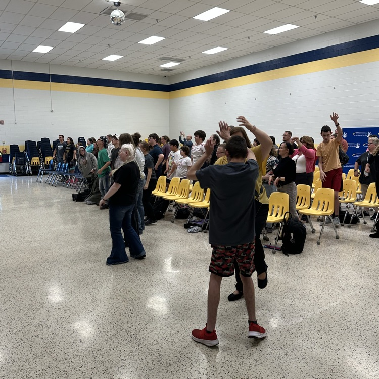 Students stand up from their yellow-colored chairs and put their arms on the air during an activity.