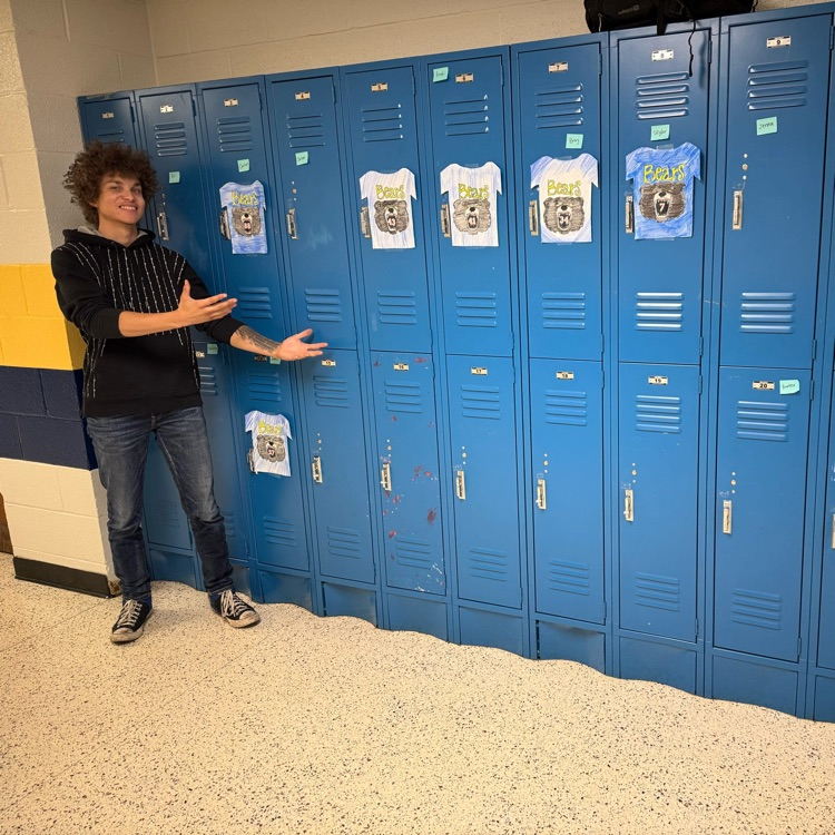 Daevon, a CAP student holds out his arms to show the display of jerseys hanging on a row of blue-colored lockers.