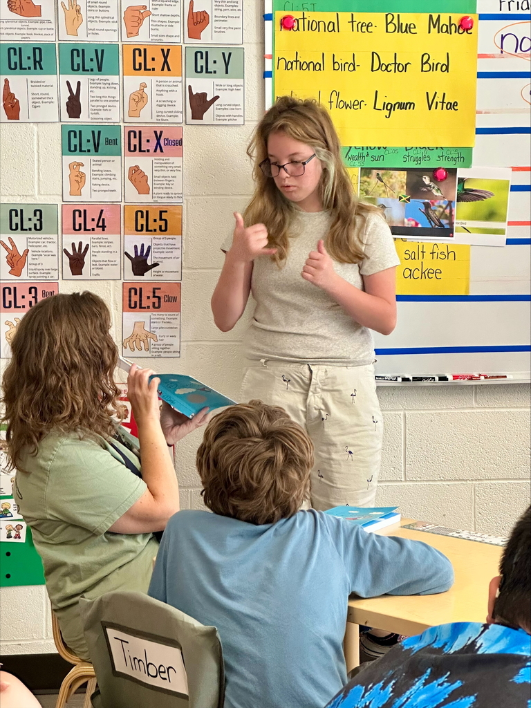 Mrs. Shoemaker holds a book while Khloe, a female student signs from the book using ASL.