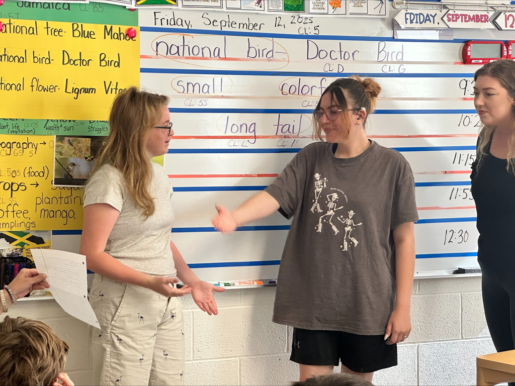 Khloe and Allyssa, two female students stand at the front of the classroom while acting out their favorite part of the book.