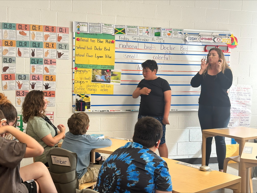 Tristian, a male student stands in front of the class acting out a portion of the book. A female ASL interpreter stands beside him.