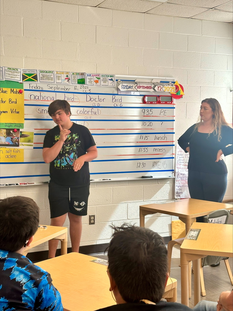 Zain, a male student stands in front of the class while using ASL.