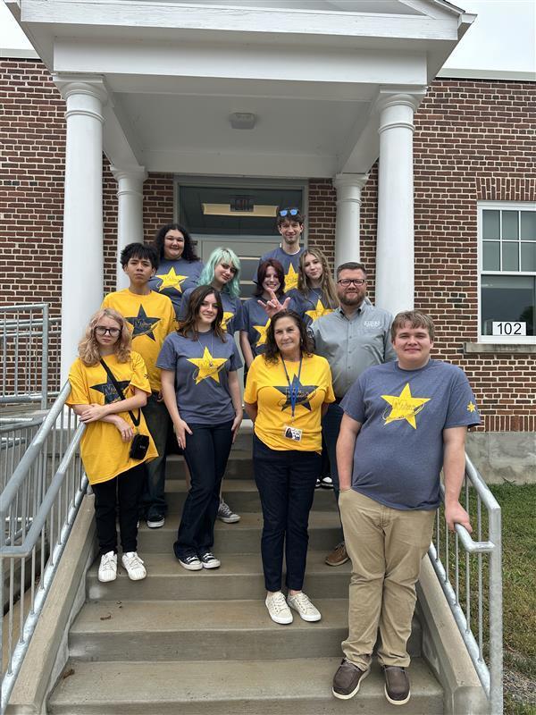Group of students standing on the steps of the Blue and Gold Building entrance with Ms. Fry and Superintendent Burch.