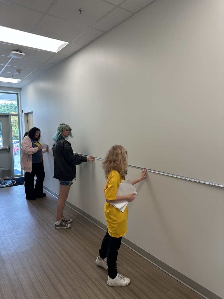 Students measure the length of a wall using a measuring tape.