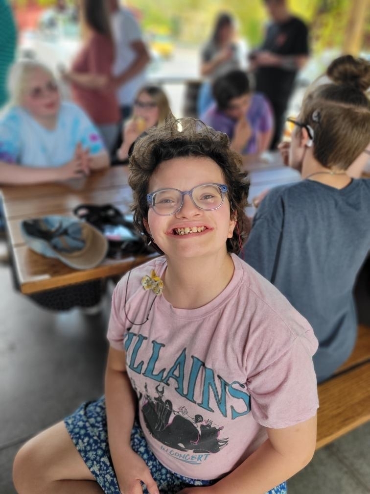 A female student wearing glasses and dark, curly hair smiles at the camera.