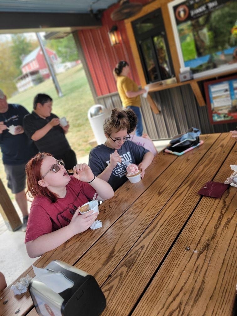Students seated at a wooden picnic table eating their ice cream.