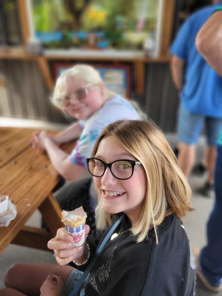 A female student wearing glasses and blonde hair smiles for the camera as she holds her ice cream cone.