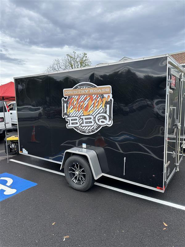 A black food truck with the name "Country Roads Blazin BBQ" written on the side of it.