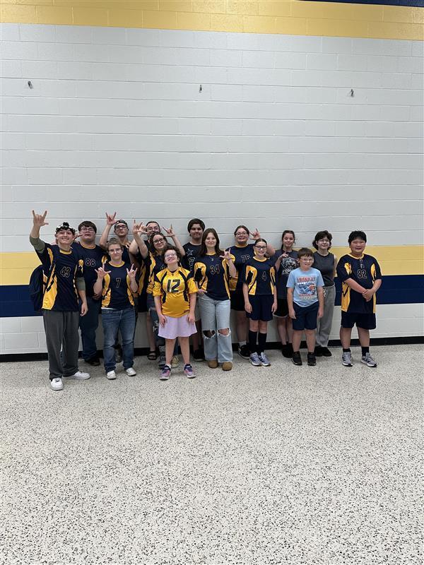 Students dressed in blue stand together for a group photo in front of a wall with blue and yellow stripes.