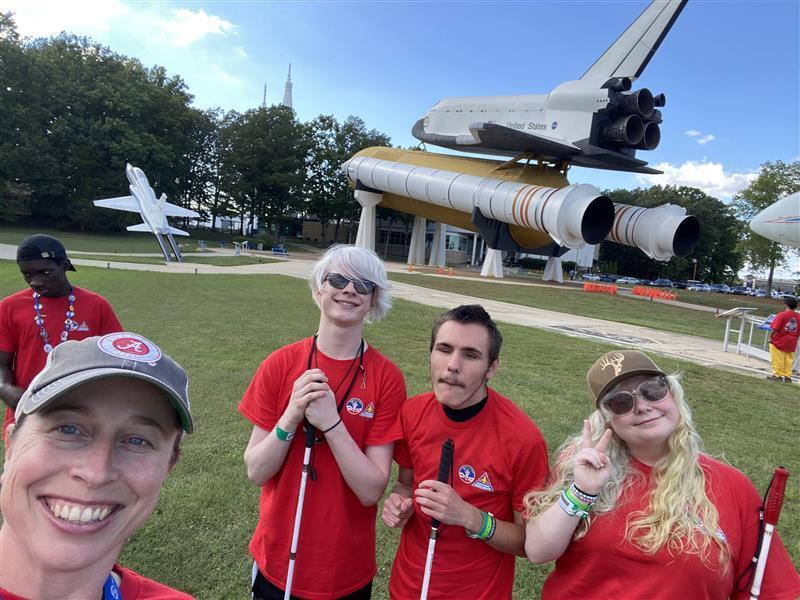 Ms. Hartman takes a selfie with the WVSDB students who attended Space Camp with a large space shuttle in the background.