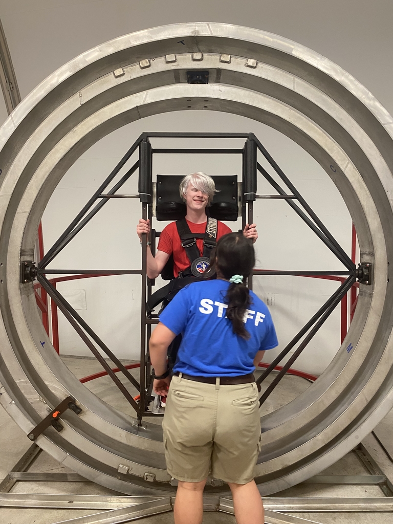 A male student wearing a red shirt sits in an astronaut simulator.