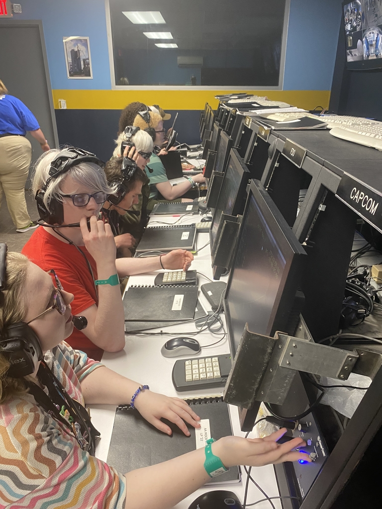 Space Camp attendees are sitting at computers while wearing headsets.