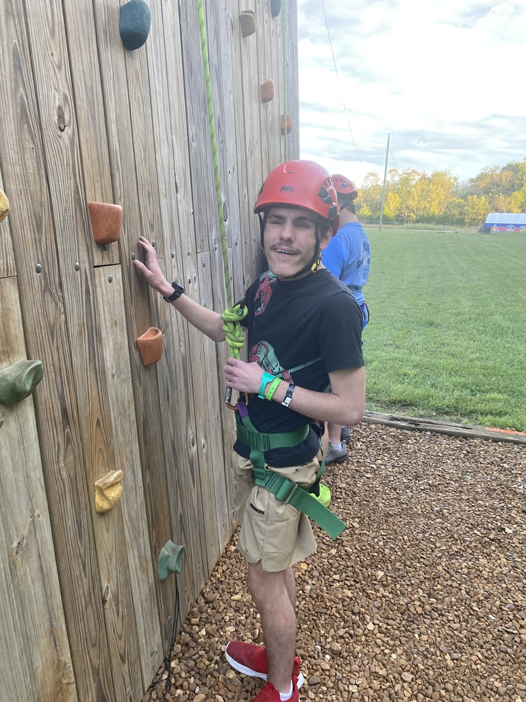 A male student smiles for the camera as he prepares to participate in a rock-climbing activity.
