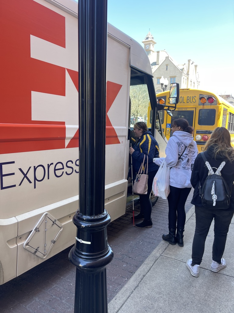 Three students stand outside of a white Fed-Ex truck that is parked next to a sidewalk.