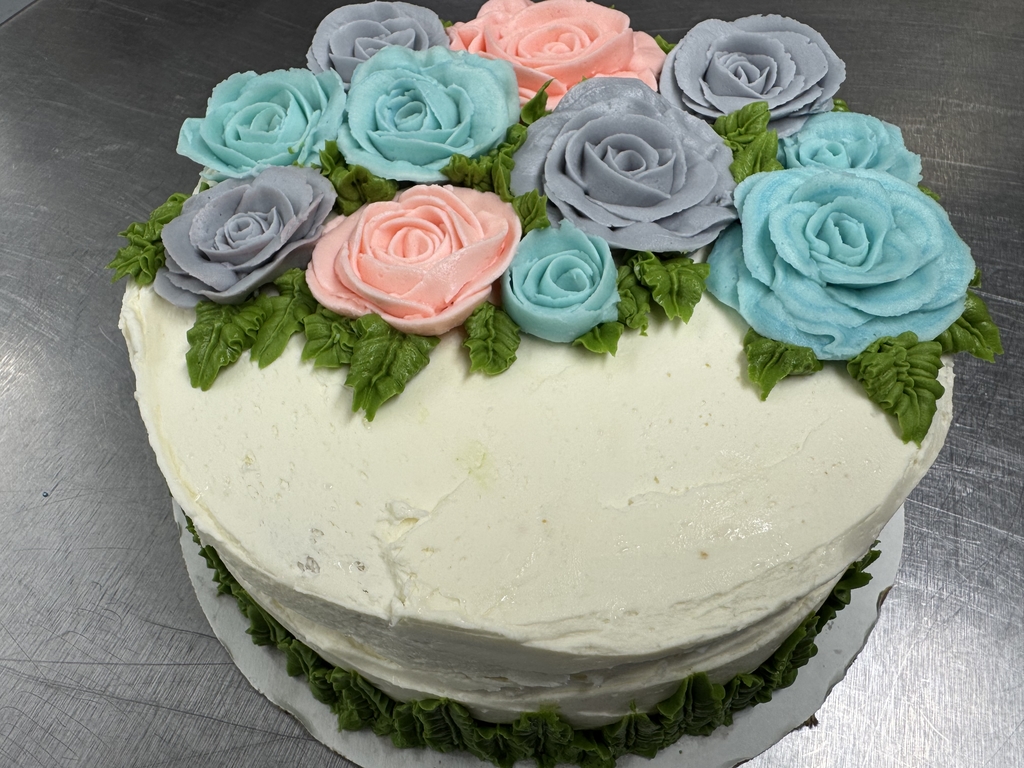 A white cake with purple, pink, and blue colored flowers with greenery accents.