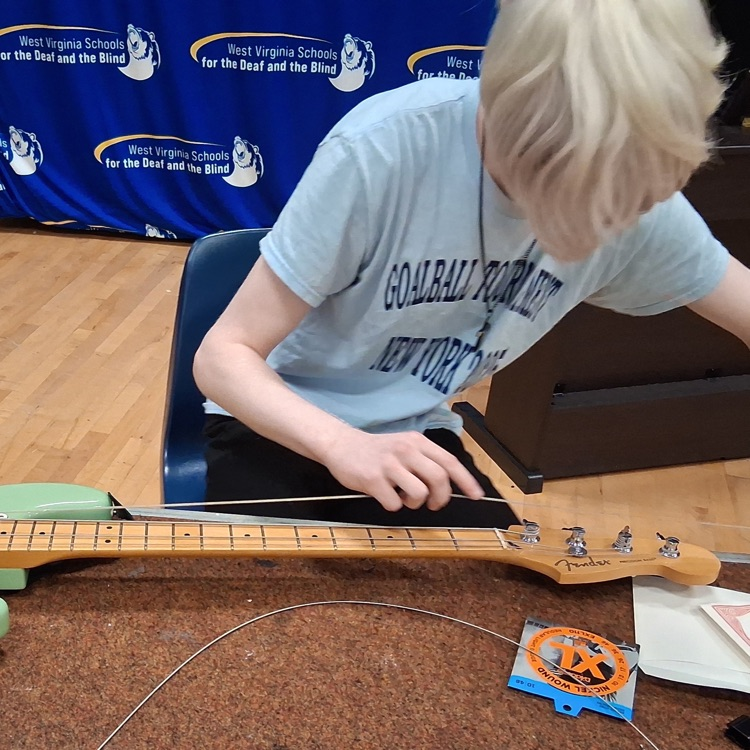 A male student looks down as he concentrates on stringing a green-colored electric guitar.