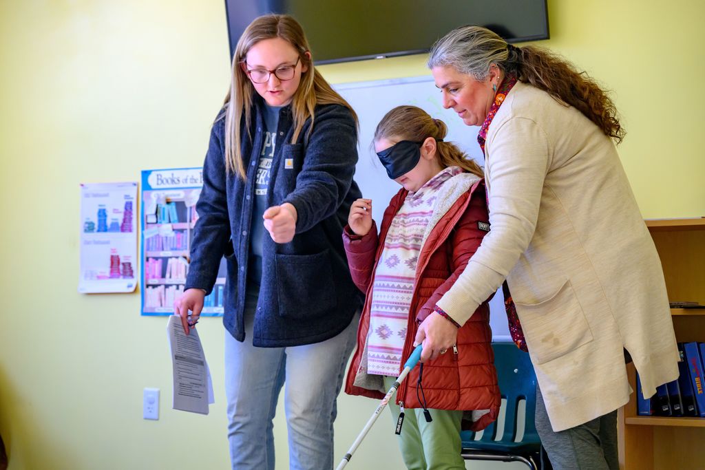 Two females assist a female student with using and navigating with her white cane.