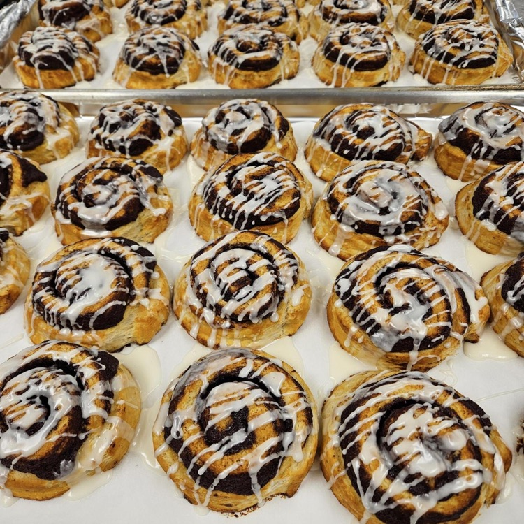 Two baking trays full of cinnamon rolls with icing drizzled on top.