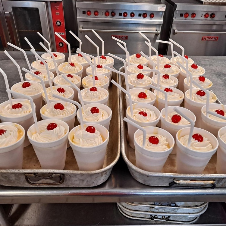 Two trays full of a dessert with whipped cream and a cherry on top.