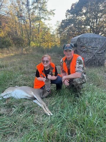 A female student and a male DNR officer pose for a photo with a deer.