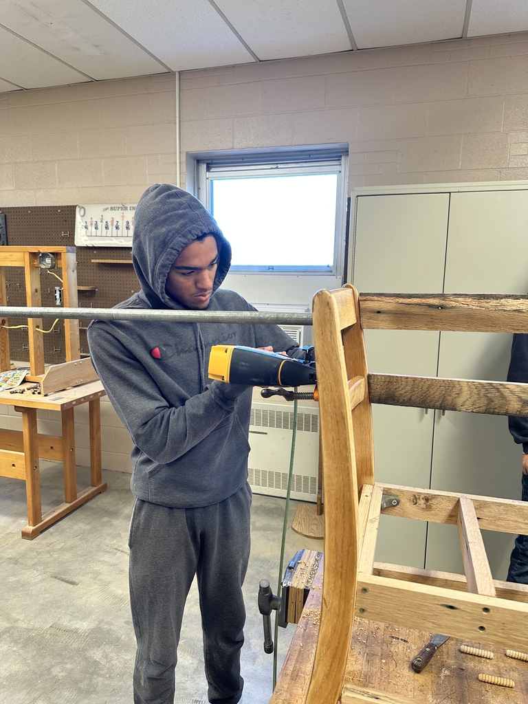 A male student uses a nail gun on a bench they are building.