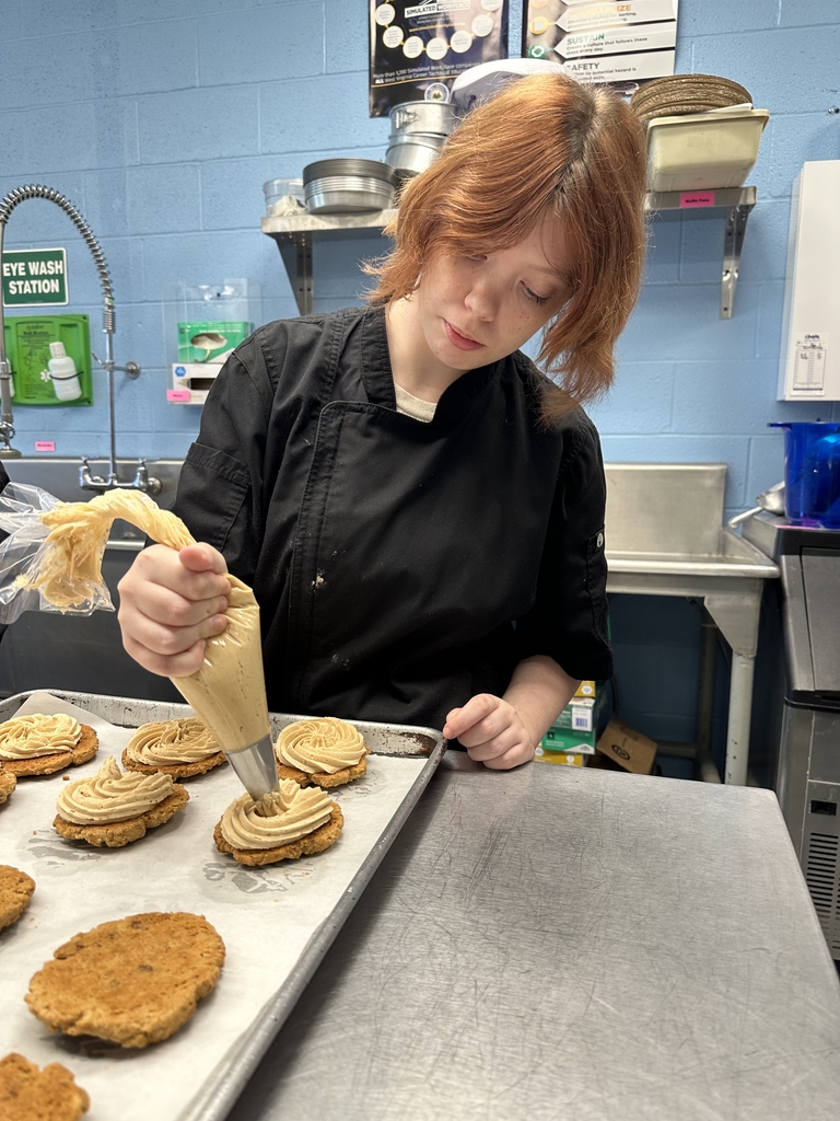 A female student concentrates as she puts frosting on a cookie.