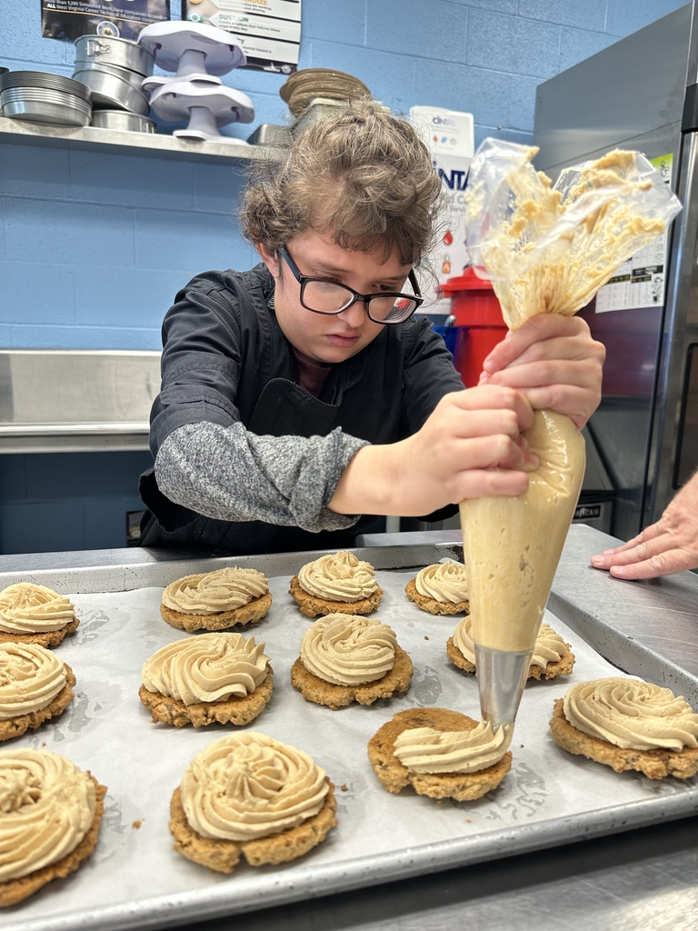 A female student concentrates as she puts frosting on a cookie.