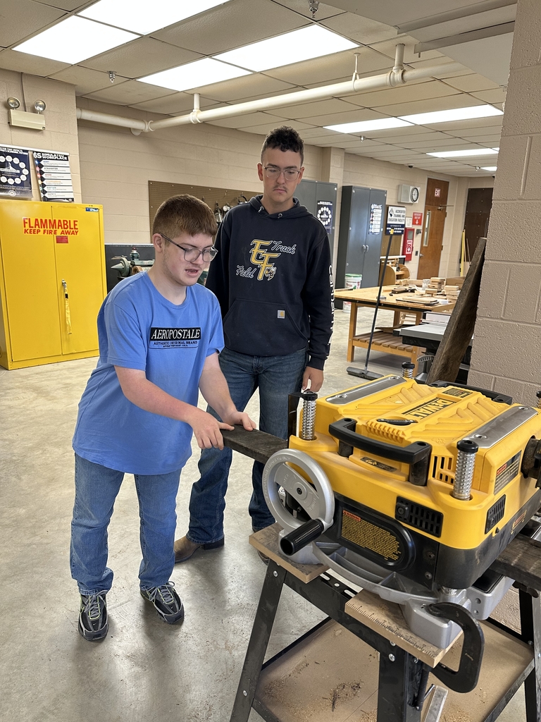 Two male students work together using a carpentry machine.