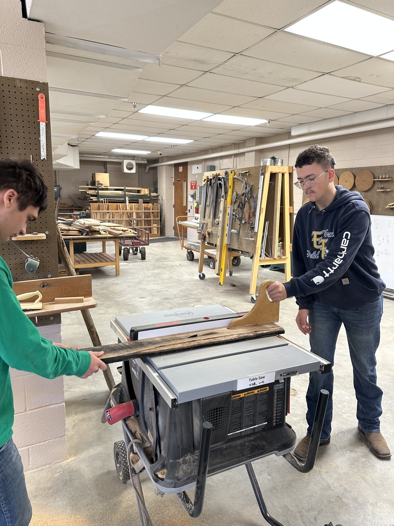 Two male students work together using a table saw.