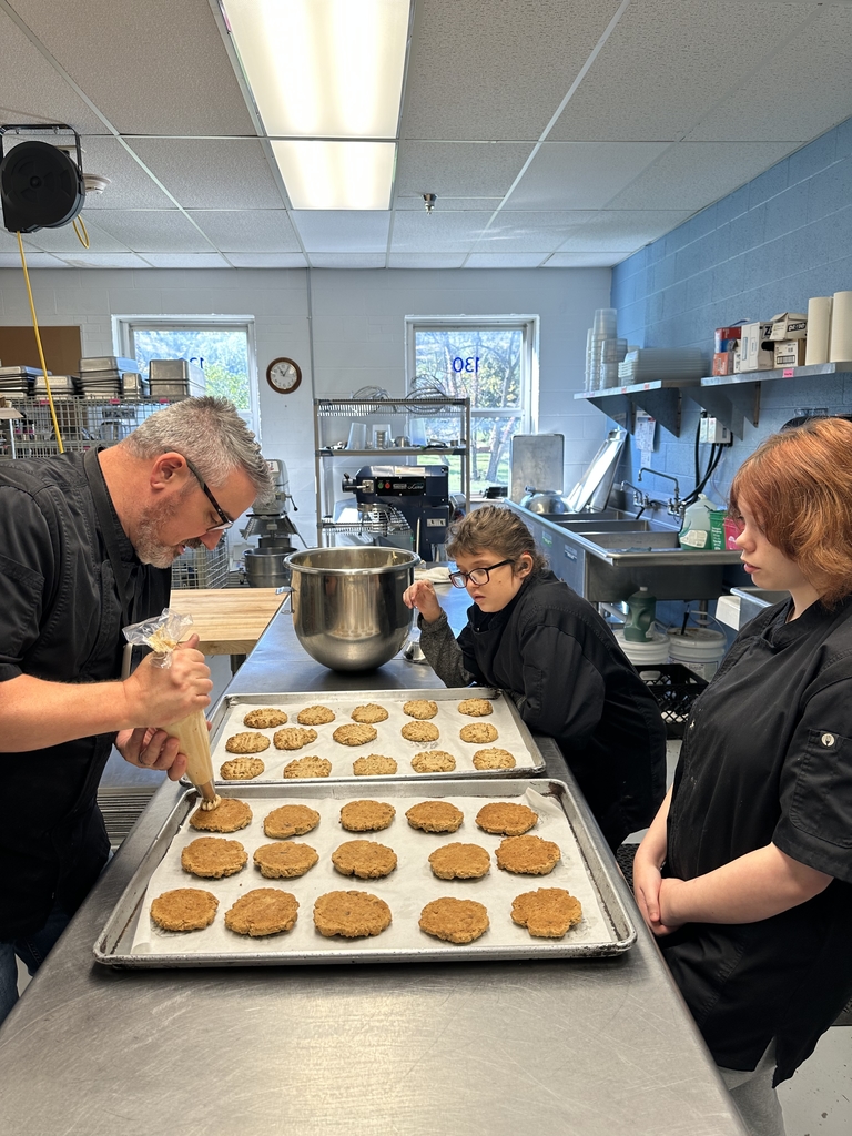 Chef Brian Olden demonstrates how to properly put frosting on a cookie to two female students.