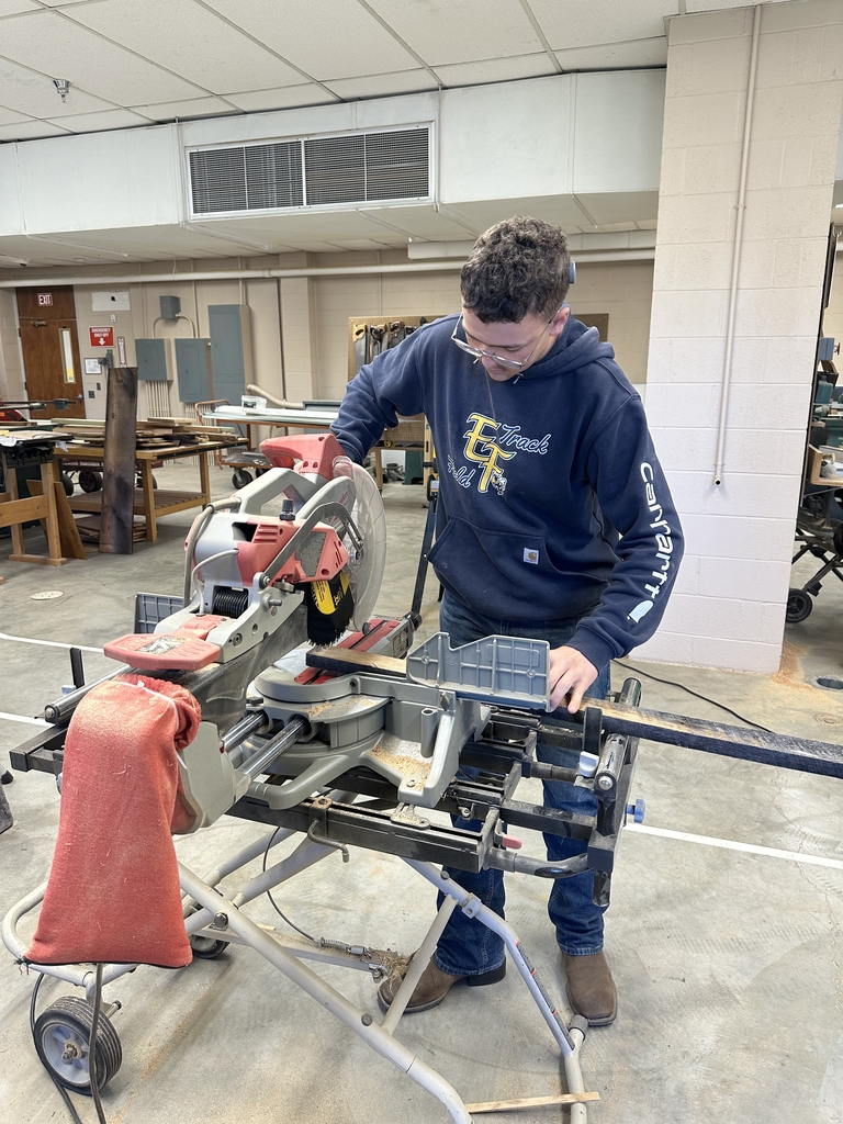A male student looks down as he uses a table saw.