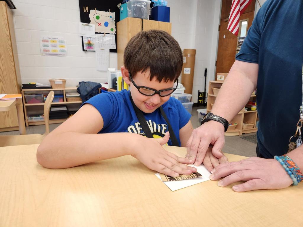 A male student looks down and smiles as he sands a part of the rocket before it is assembled.
