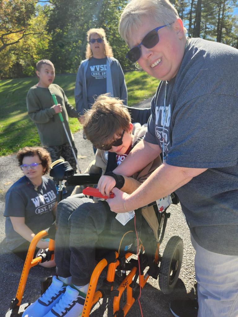 Ms. Biddle smiles for the camera as she assists a male student in a wheelchair press the rocket launch button.