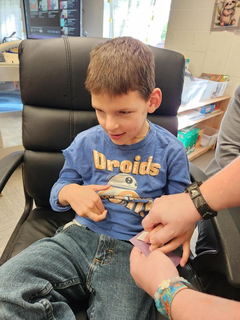 A male student is seated as he receives help sanding a part of the rocket from a female teacher's aide.