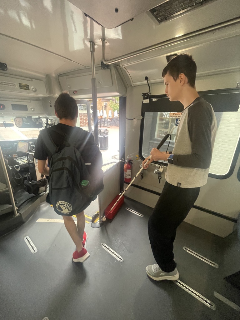Two male students use their white canes to navigate getting off of a bus.