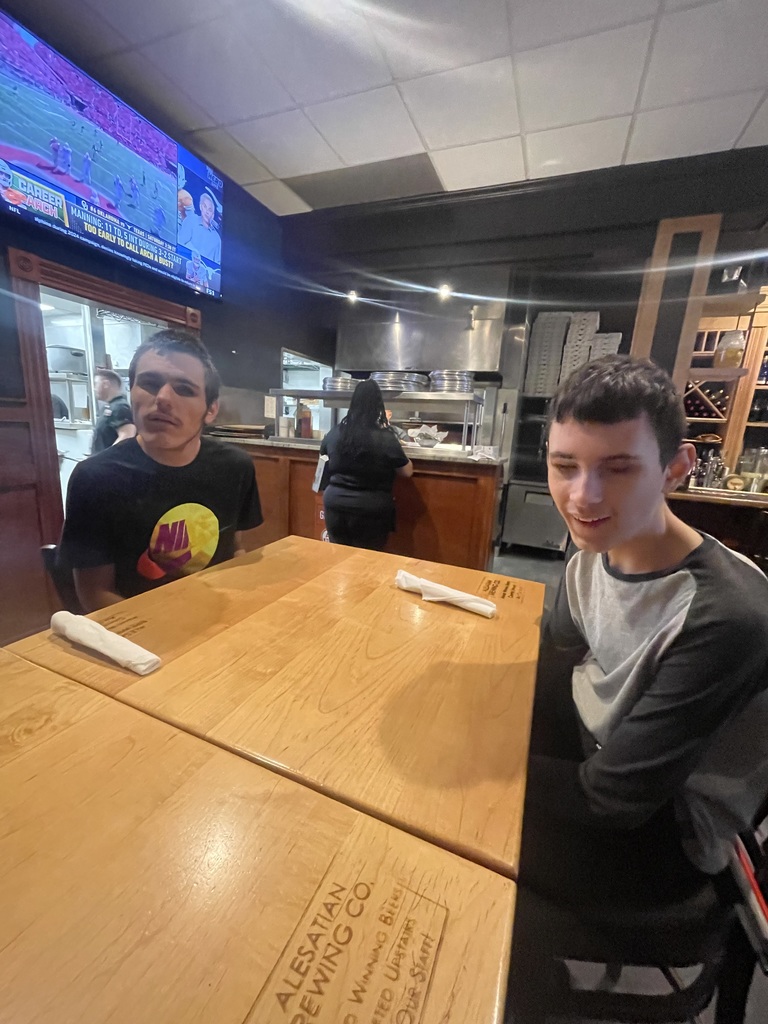 Two male students seated at a table in a restaurant smile for the camera.